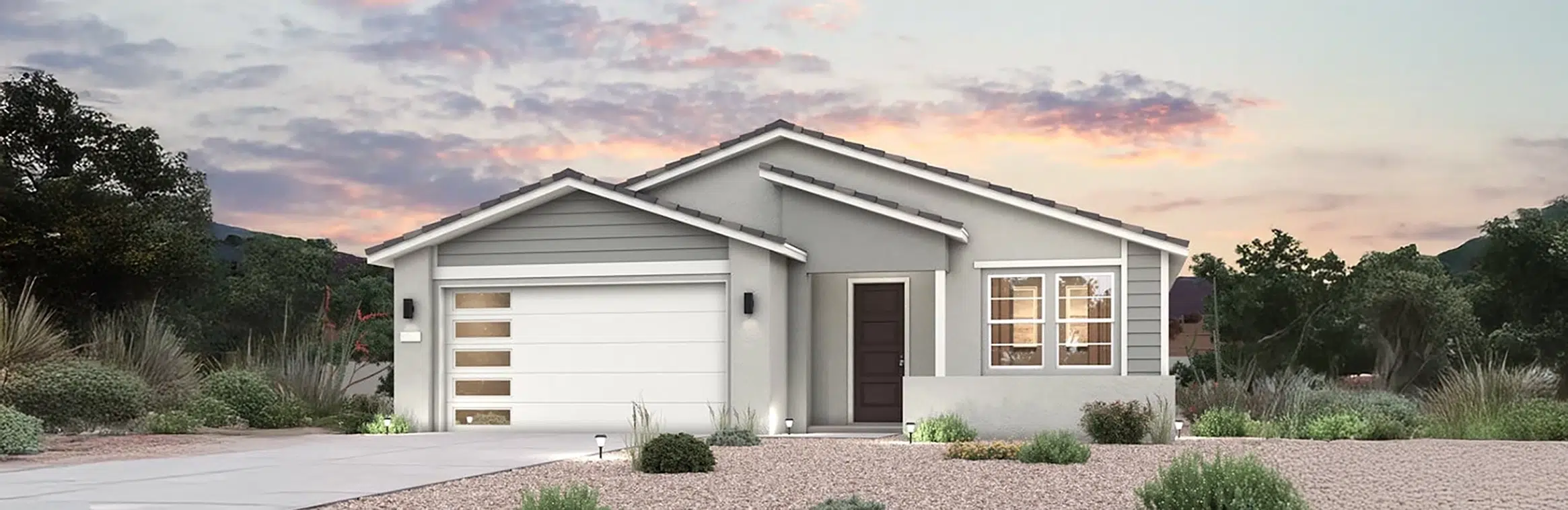 Single-story modern house with gray and white exterior, double garage, front door, and landscaped yard with gravel and desert plants at sunset.