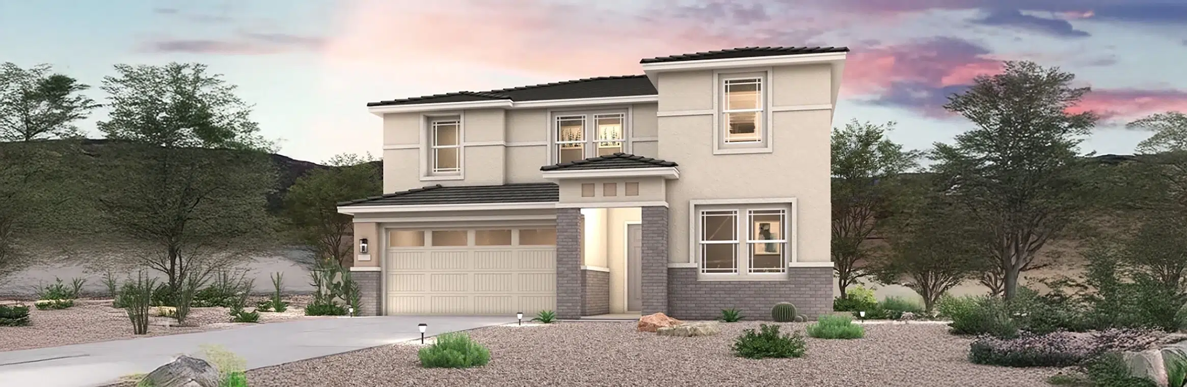 Two-story modern house with light-colored walls, brick accents, and large windows, set in a desert landscape with rocks and sparse vegetation at sunset.