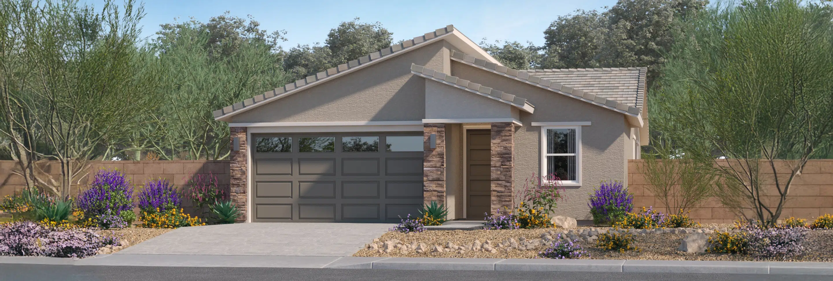 Single-story house with a two-car garage, stone columns, and desert landscaping featuring shrubs and purple flowers, enclosed by a wooden fence.