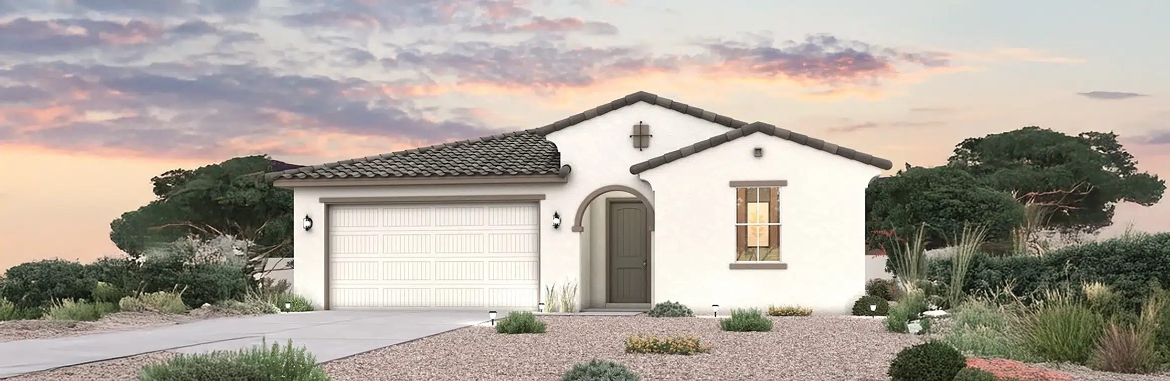 A single-story house with a tile roof, white stucco exterior, arched front door, attached garage, and desert landscaping at sunset.