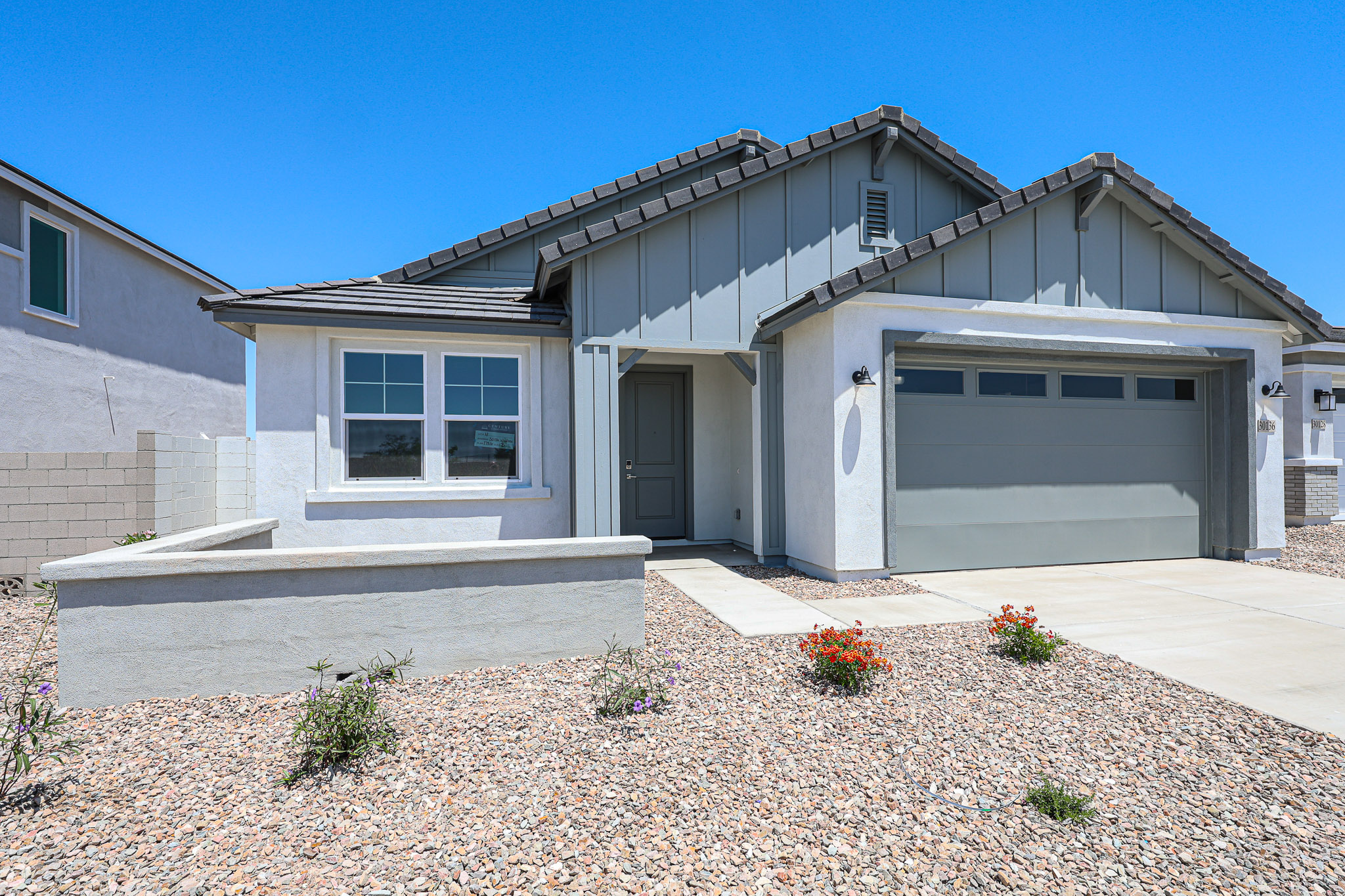Single-story modern house with a gray garage door, white walls, and a rock landscape under a clear blue sky.