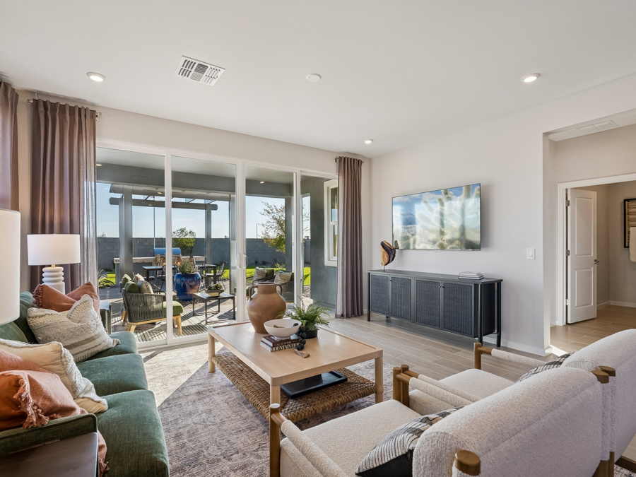 Modern living room with neutral furniture, a coffee table, wall-mounted TV, large windows, and sliding glass doors leading to a covered patio and backyard.