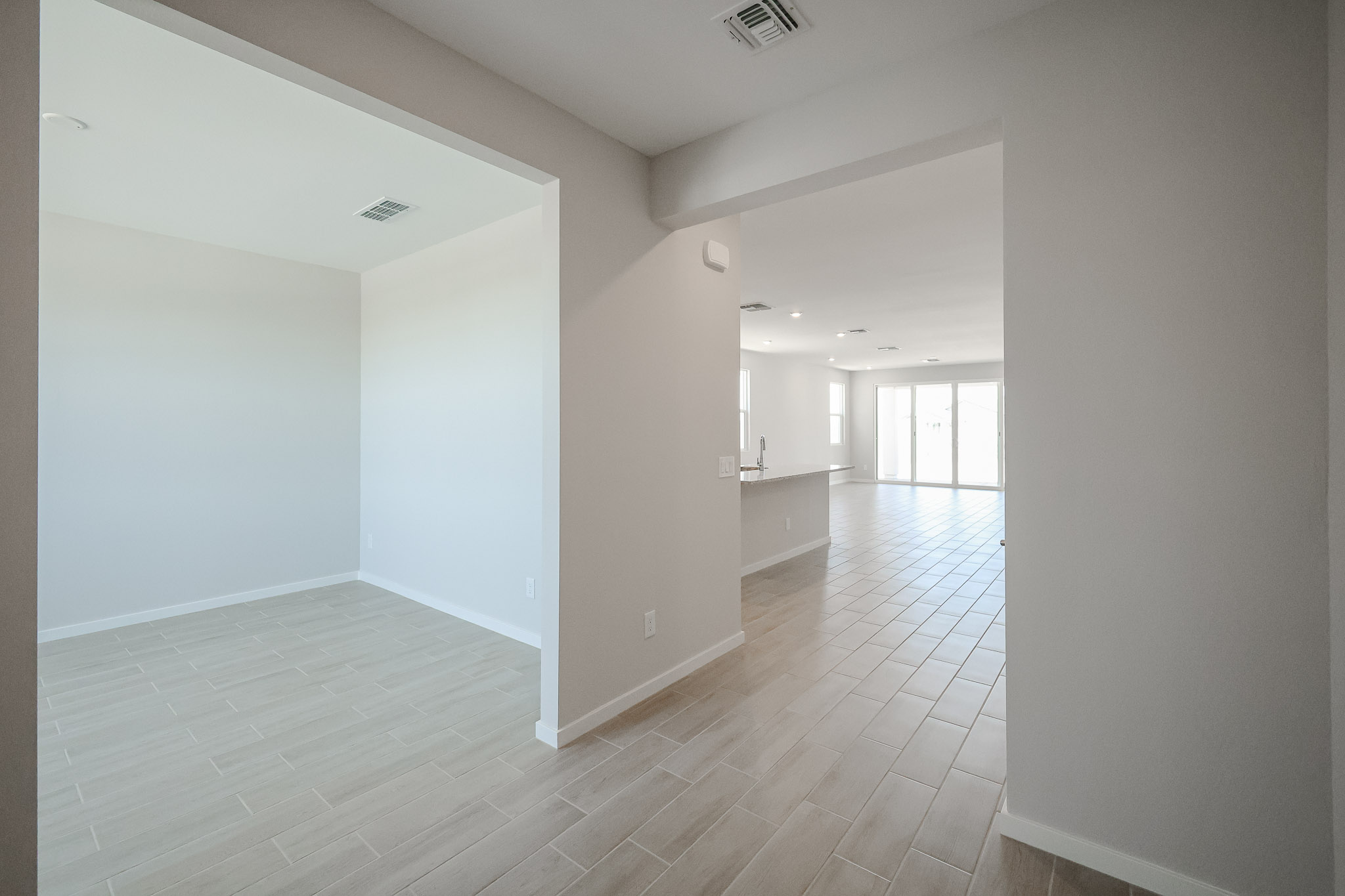 Empty modern interior with tiled floors, white walls, and large windows letting in natural light. Open layout connects multiple rooms.