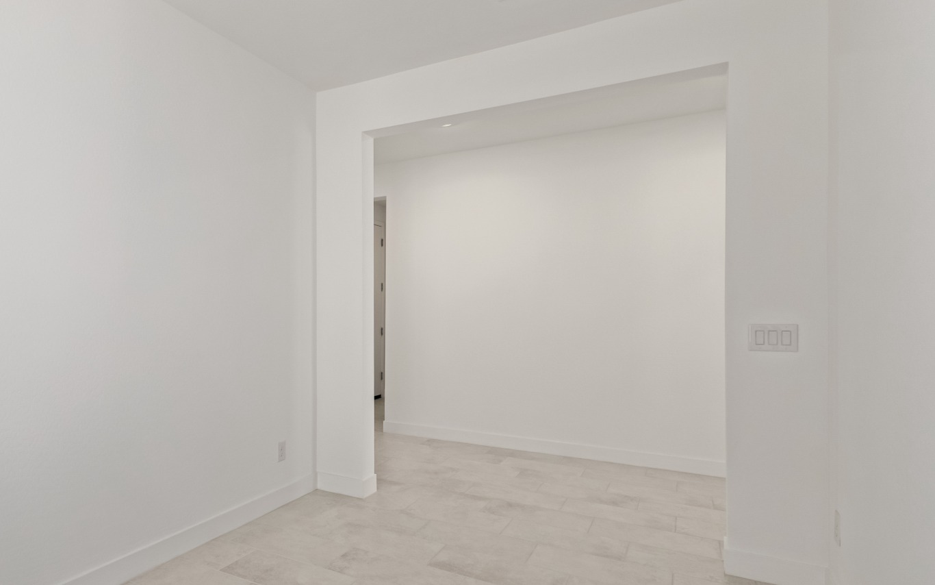 A view into an empty room with white walls, tiled flooring, and a light switch on the wall.