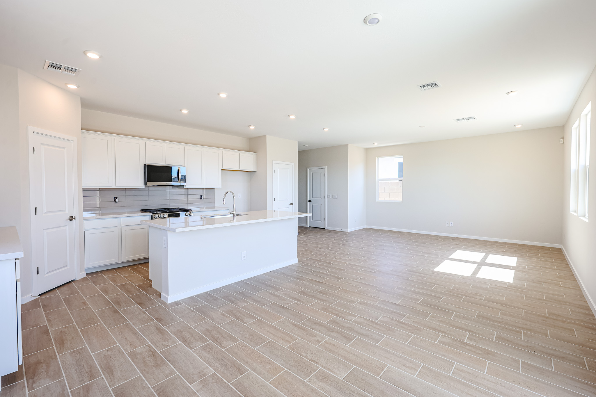 Spacious, unfurnished open-plan kitchen and living area with white cabinets, tile flooring, and large windows letting in natural light.