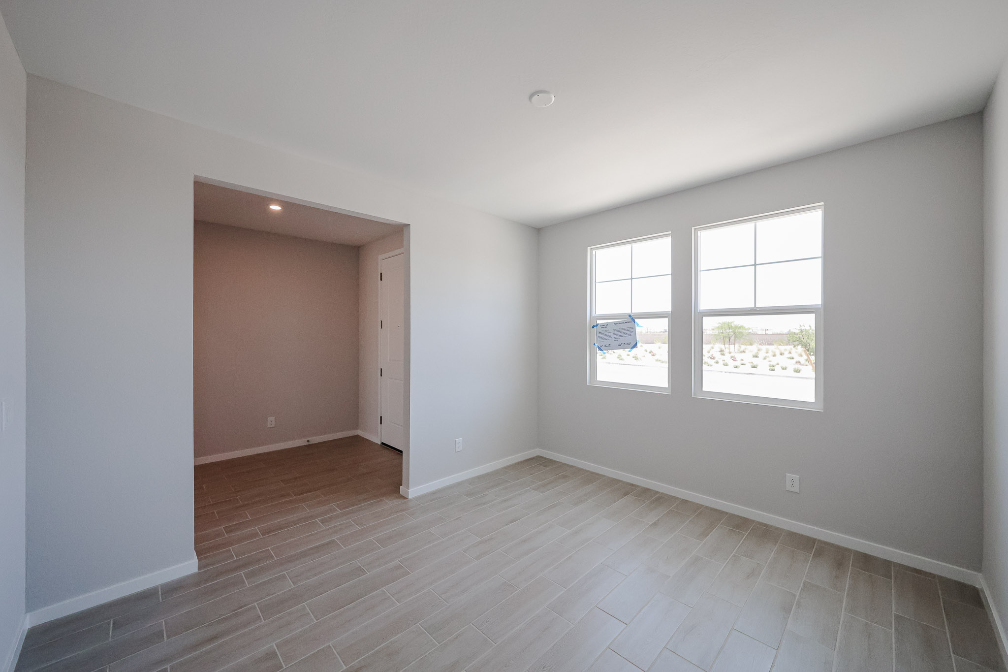 Empty room with light-colored tile flooring, white walls, two windows, and an open doorway leading to a small hallway with a closet.
