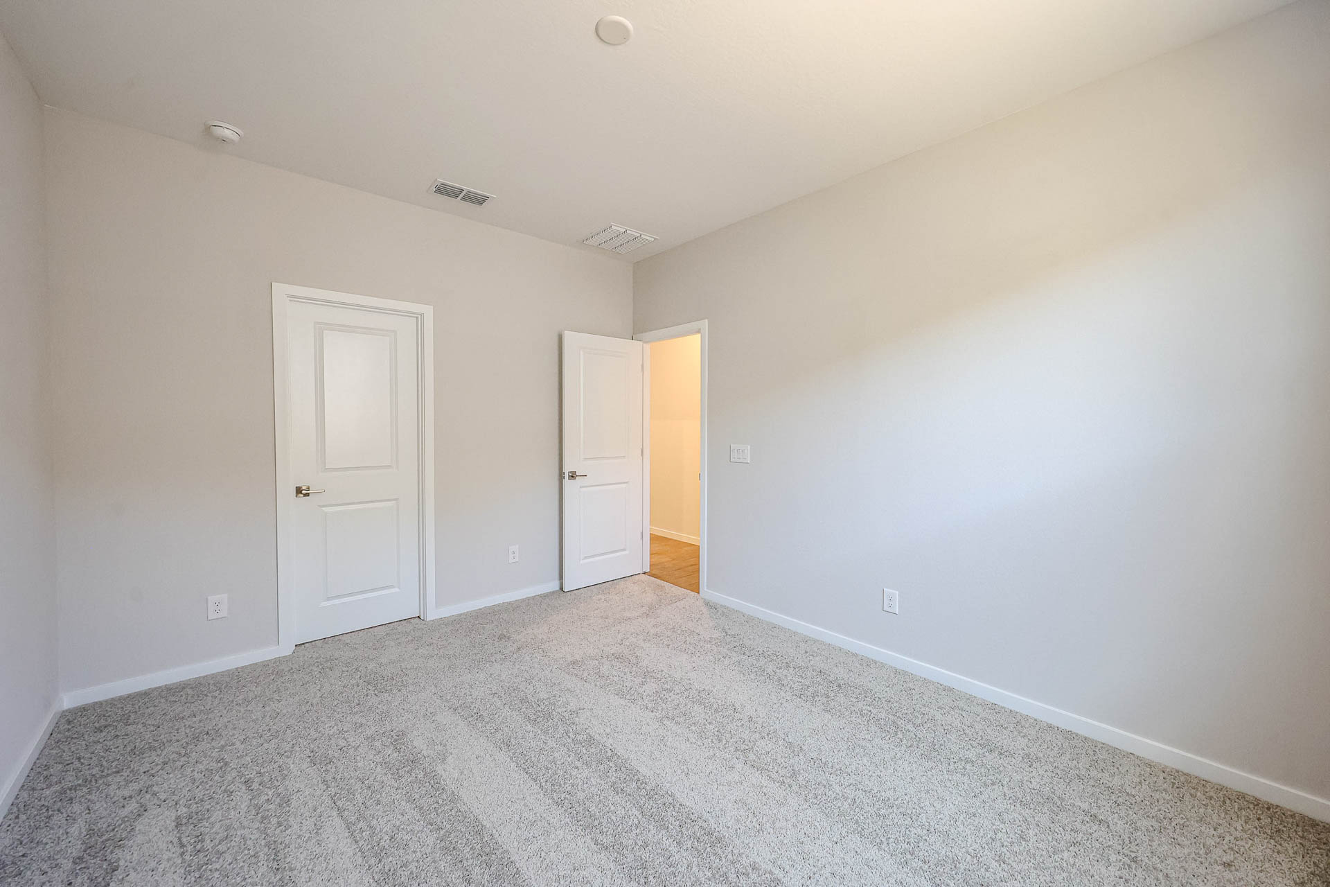 Empty room with light beige carpet, white walls, two closed white doors, one open door, and overhead lighting.