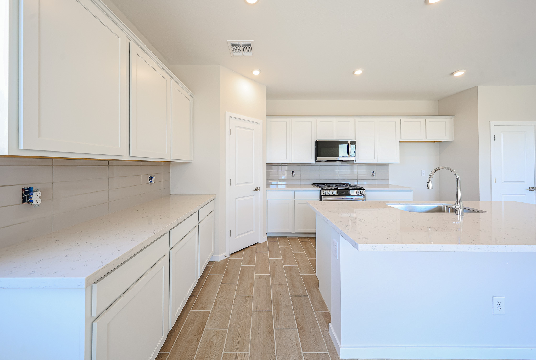 Modern kitchen with white cabinets, light countertops, wood-look tile flooring, an island with a sink, and built-in appliances. The space is clean, bright, and minimalistic.
