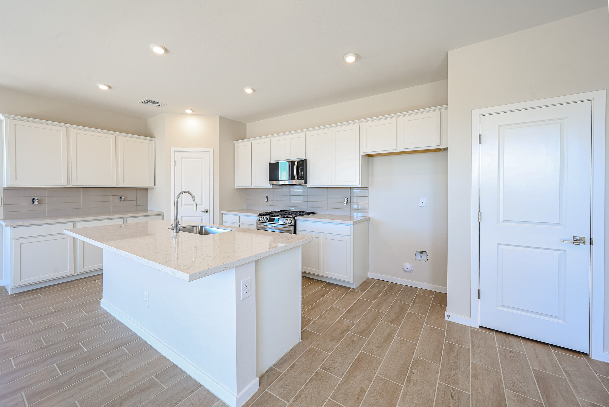 Modern kitchen with light wood tile flooring, white cabinets, stainless steel appliances, a kitchen island with sink, and neutral-colored walls.