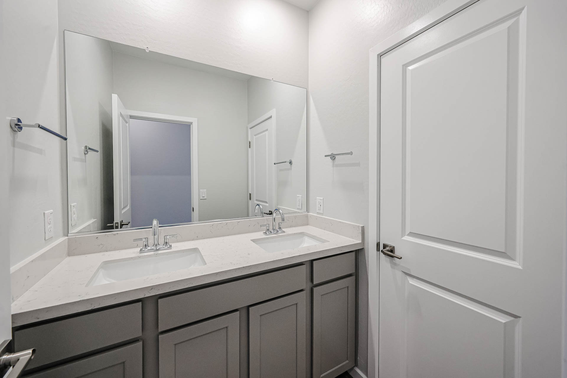 Modern bathroom with a double-sink vanity, white countertops, two mirrors, and two doors; silver faucets and handles, neutral color scheme.