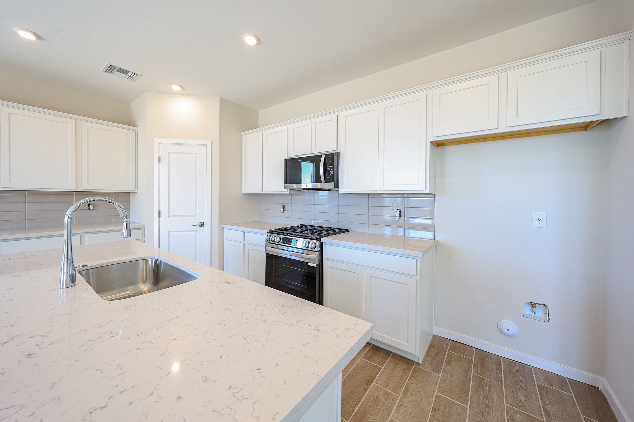 Modern kitchen with white cabinets, stainless steel appliances, a built-in sink on a quartz island, beige tile flooring, and space for a washer or dryer on the right wall.
