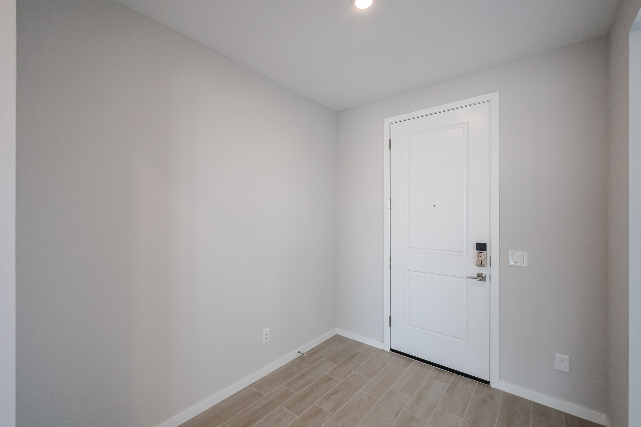 A simple entryway with light beige tiled floor, white walls, and a closed white door with a modern handle and lock.