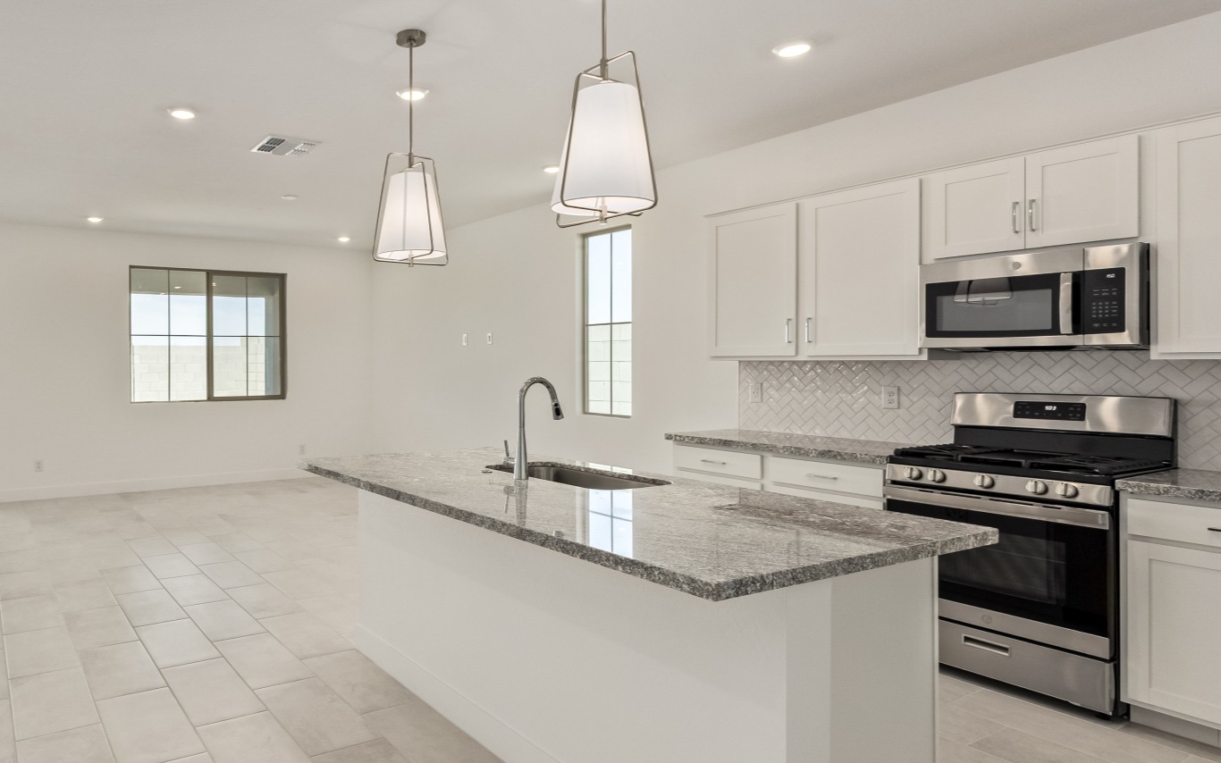 Modern kitchen with white cabinetry, a granite-topped island with a sink, and stainless steel appliances.