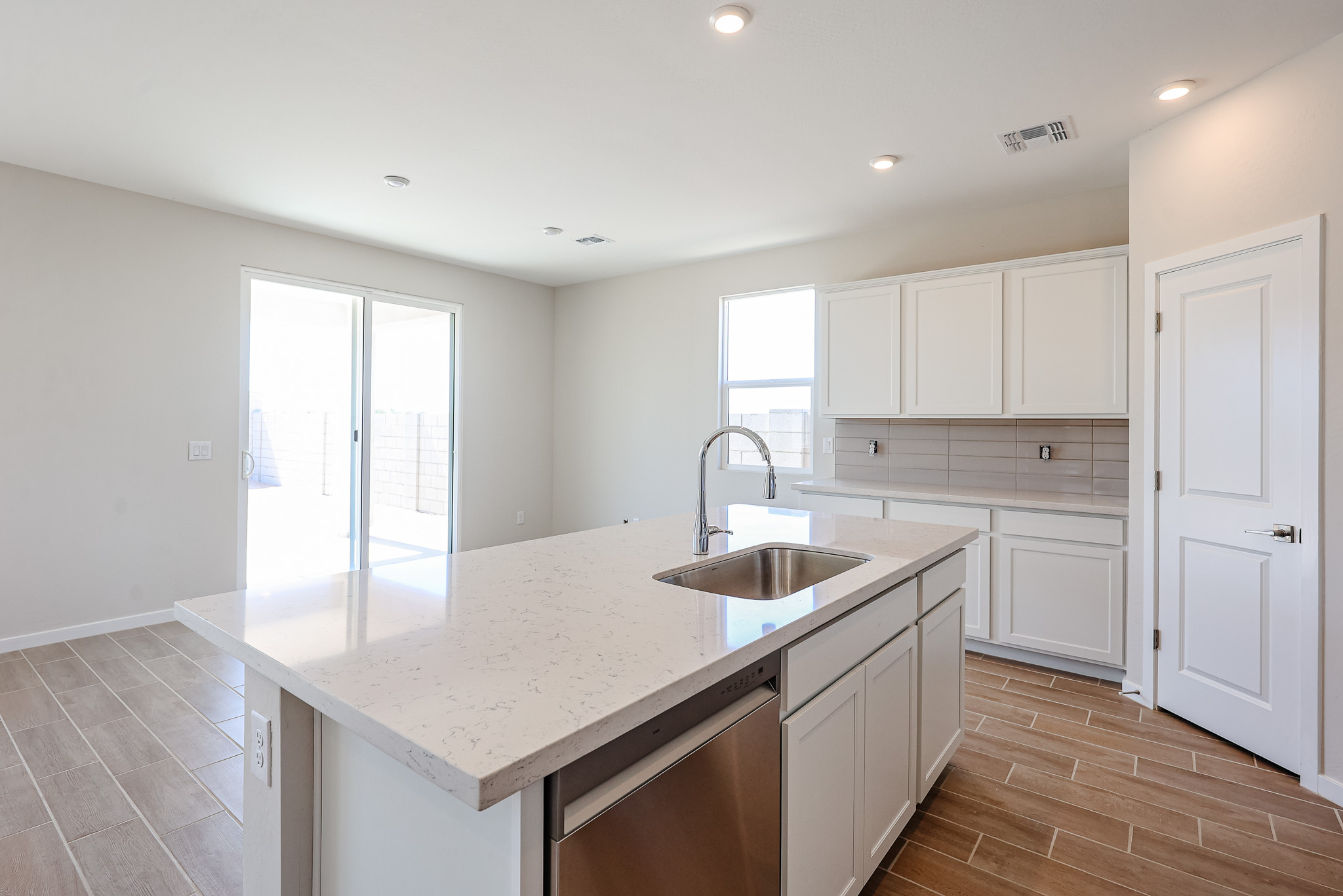 Modern kitchen with white cabinets, marble island with sink, stainless steel dishwasher, tile flooring, and sliding glass doors leading to a fenced backyard.