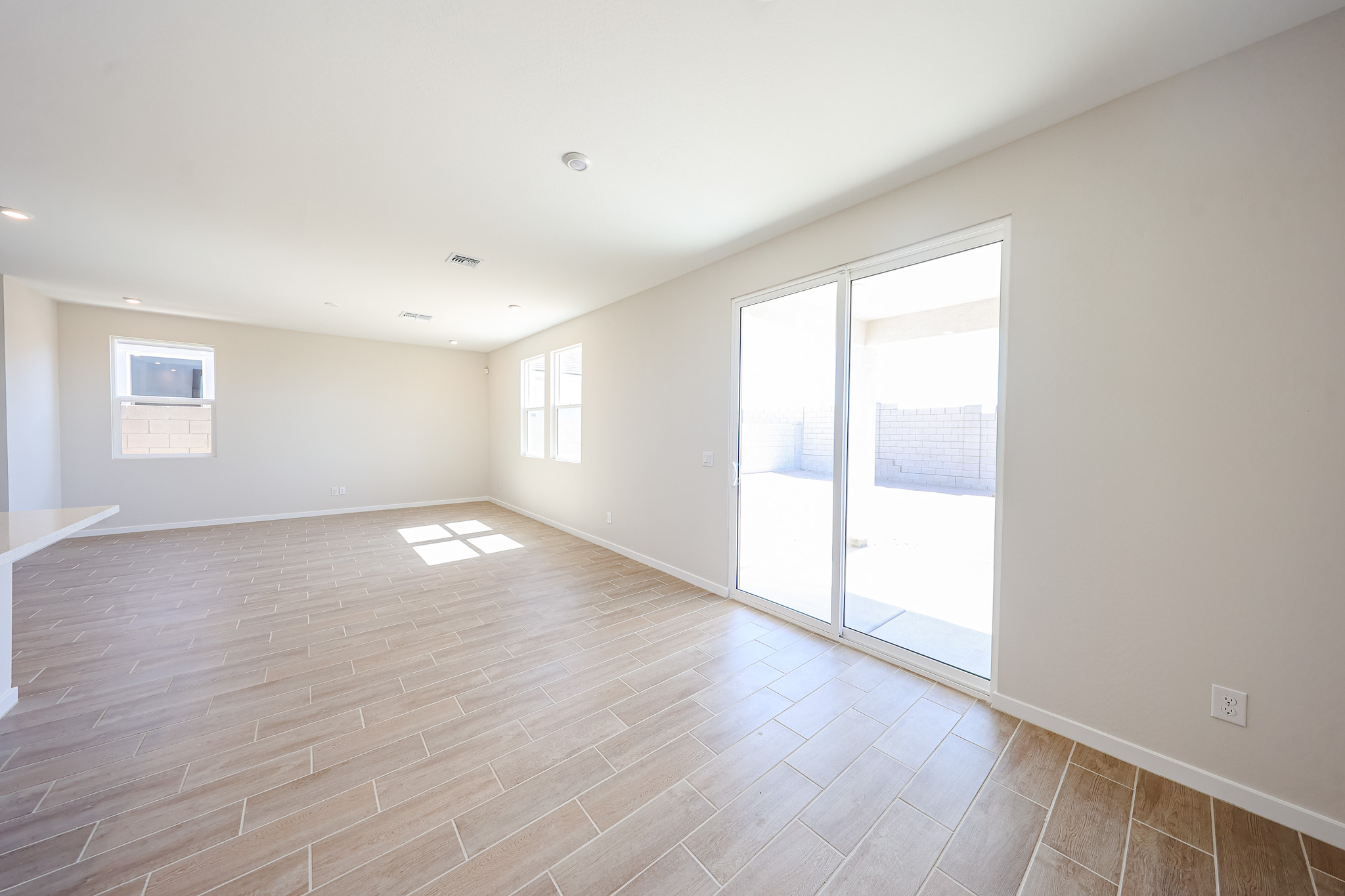 Empty room with light wood tile flooring, beige walls, large windows, and glass sliding door leading to a fenced backyard.