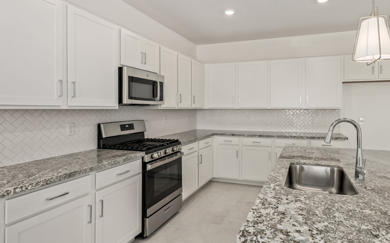 Kitchen with white cabinets, speckled granite countertops, stainless steel appliances, and a herringbone tile backsplash.