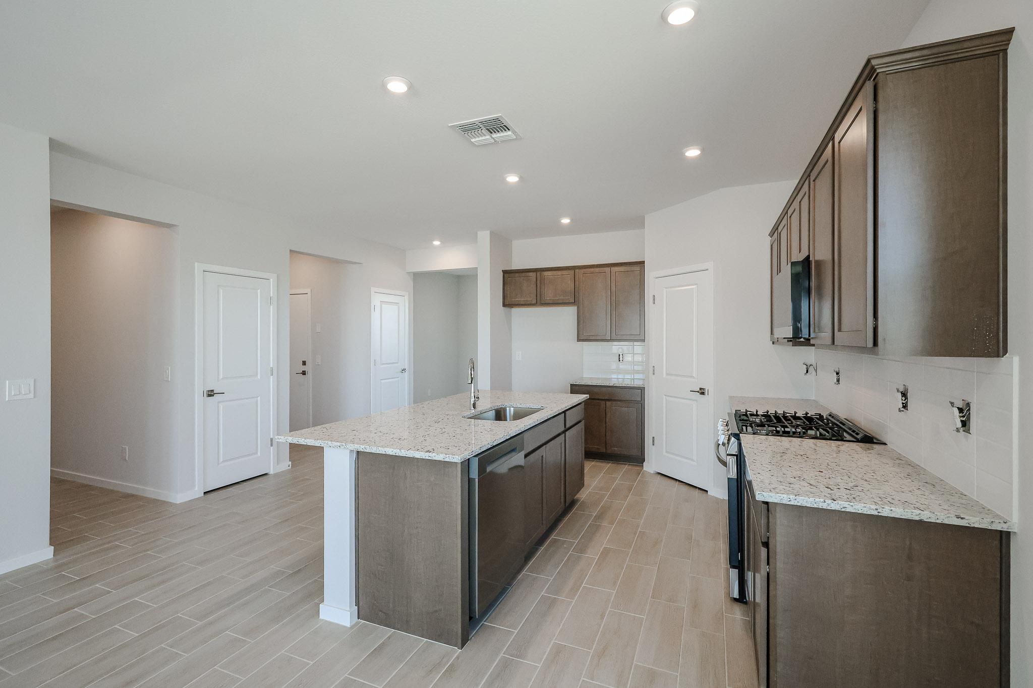 Modern kitchen with wood cabinets, granite countertops, center island with sink, gas stove, tile flooring, and recessed lighting. White walls and doors complete the space.