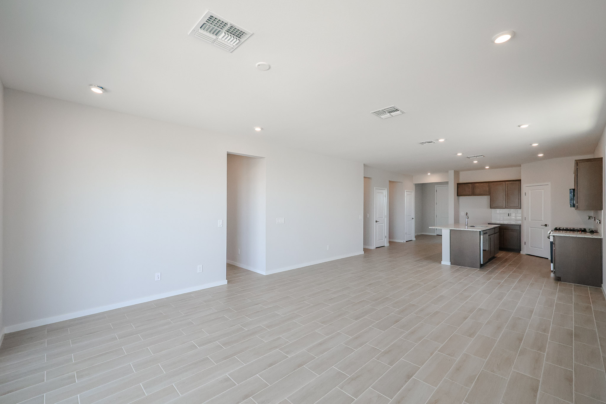 Spacious, unfurnished open-plan living area with tiled floor, recessed lighting, and a modern kitchen featuring an island and stainless steel appliances.
