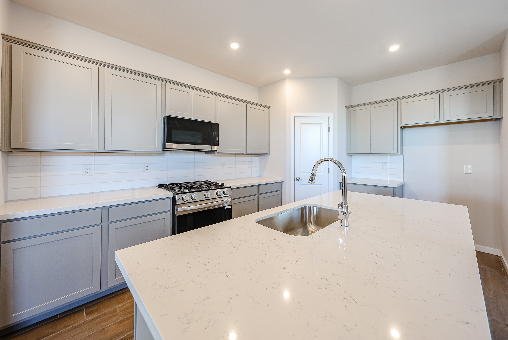 Modern kitchen with light gray cabinets, white quartz countertops, stainless steel appliances, gas stove, built-in microwave, and tile backsplash under recessed lighting.