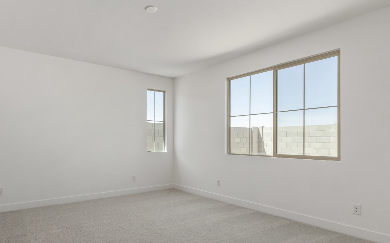 Empty room with white walls, carpeted floors, and two windows overlooking a block wall.