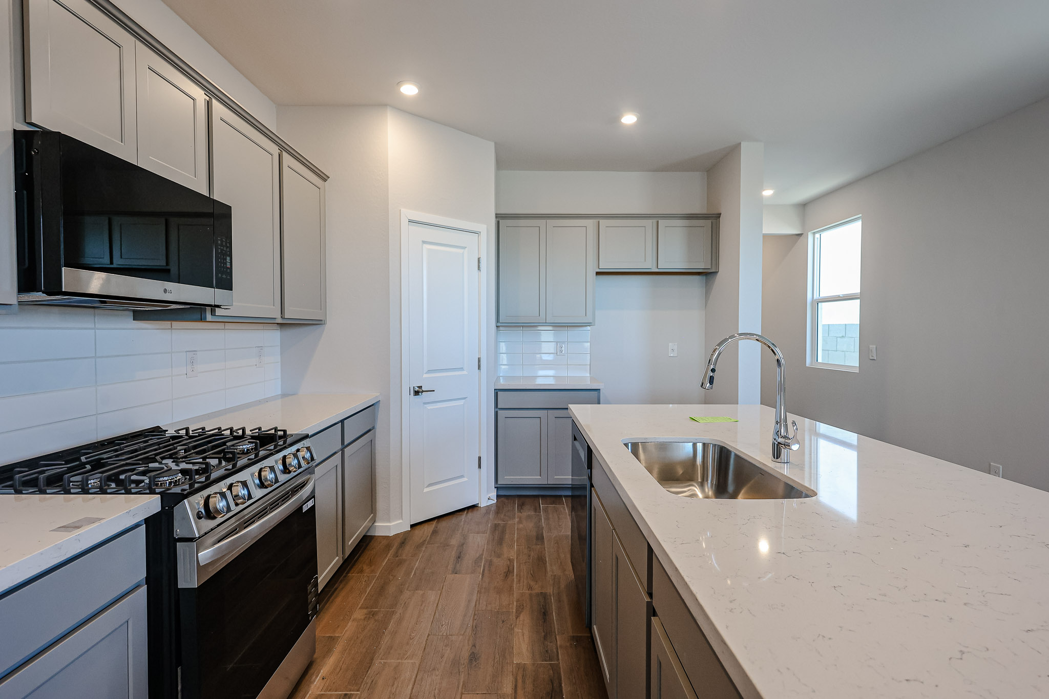 Modern kitchen with gray cabinets, stainless steel appliances, a gas stove, built-in microwave, white countertops, island sink, and wood-look flooring.