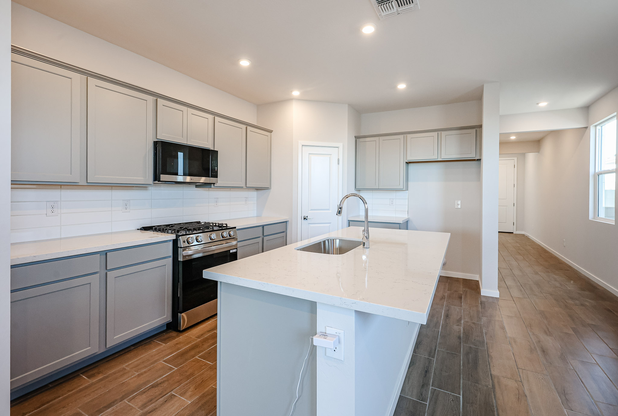 Modern kitchen with gray cabinets, stainless steel appliances, a large island with sink, tile flooring, and recessed lighting.