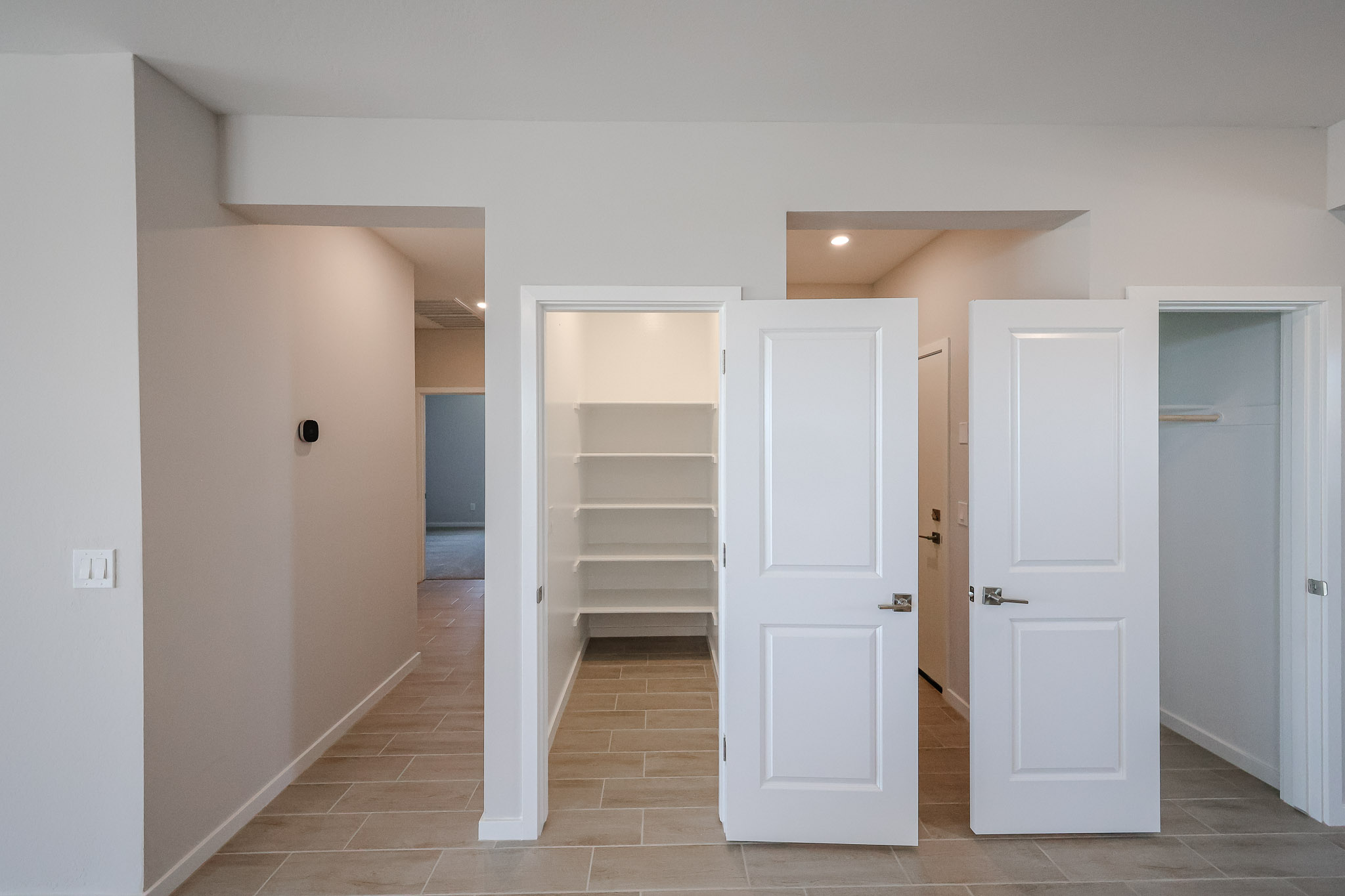A room with beige tile floor, three white doors, one open revealing shelves, another partially open, and a hallway visible to the left.
