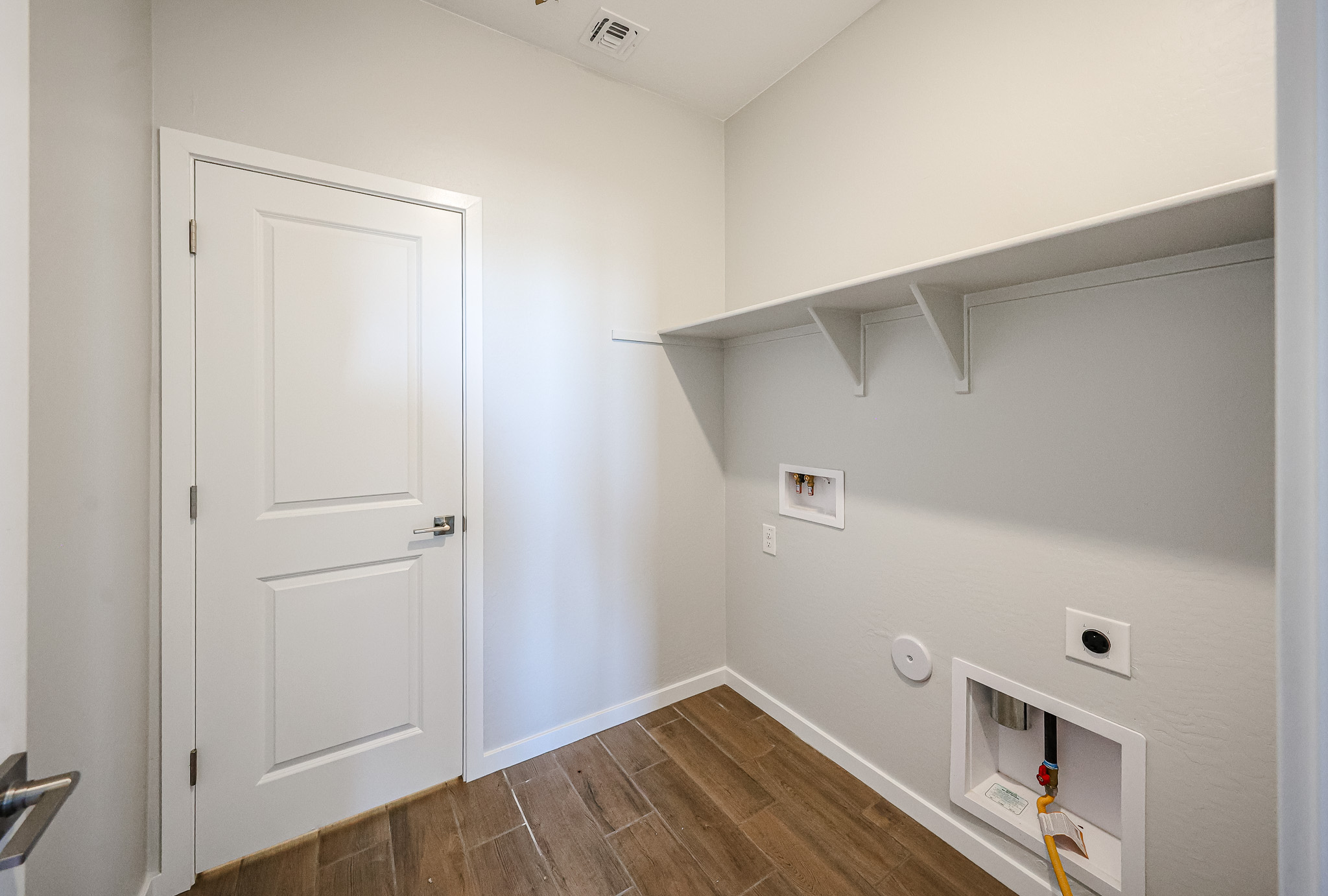 Empty laundry room with wood-look tile floor, white walls, a closed door, upper shelf, and hookups for a washer and dryer.