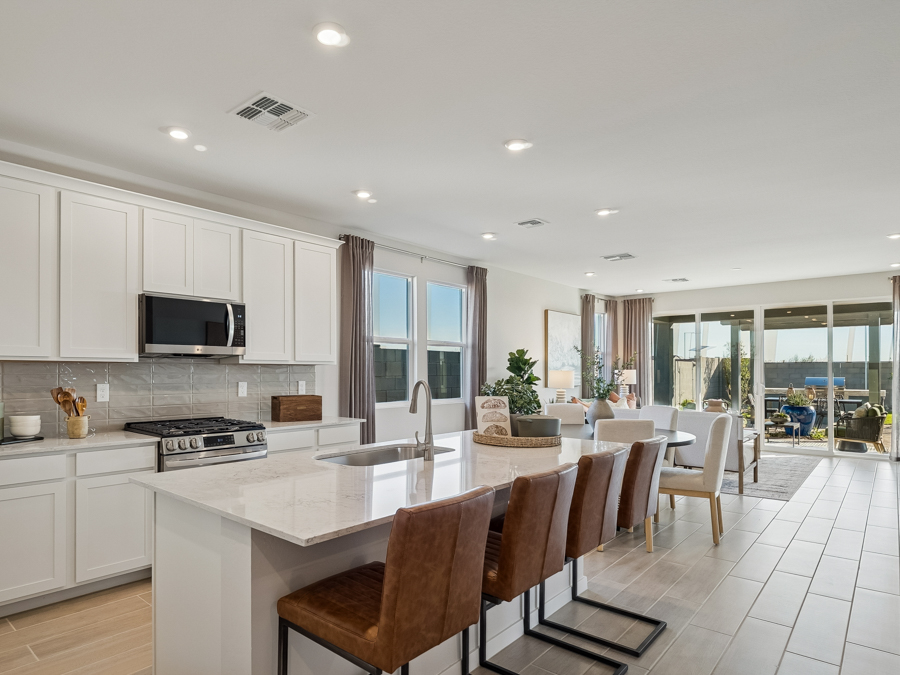 Modern open-concept kitchen and dining area with white cabinets, marble island, brown leather stools, and large windows leading to a patio.