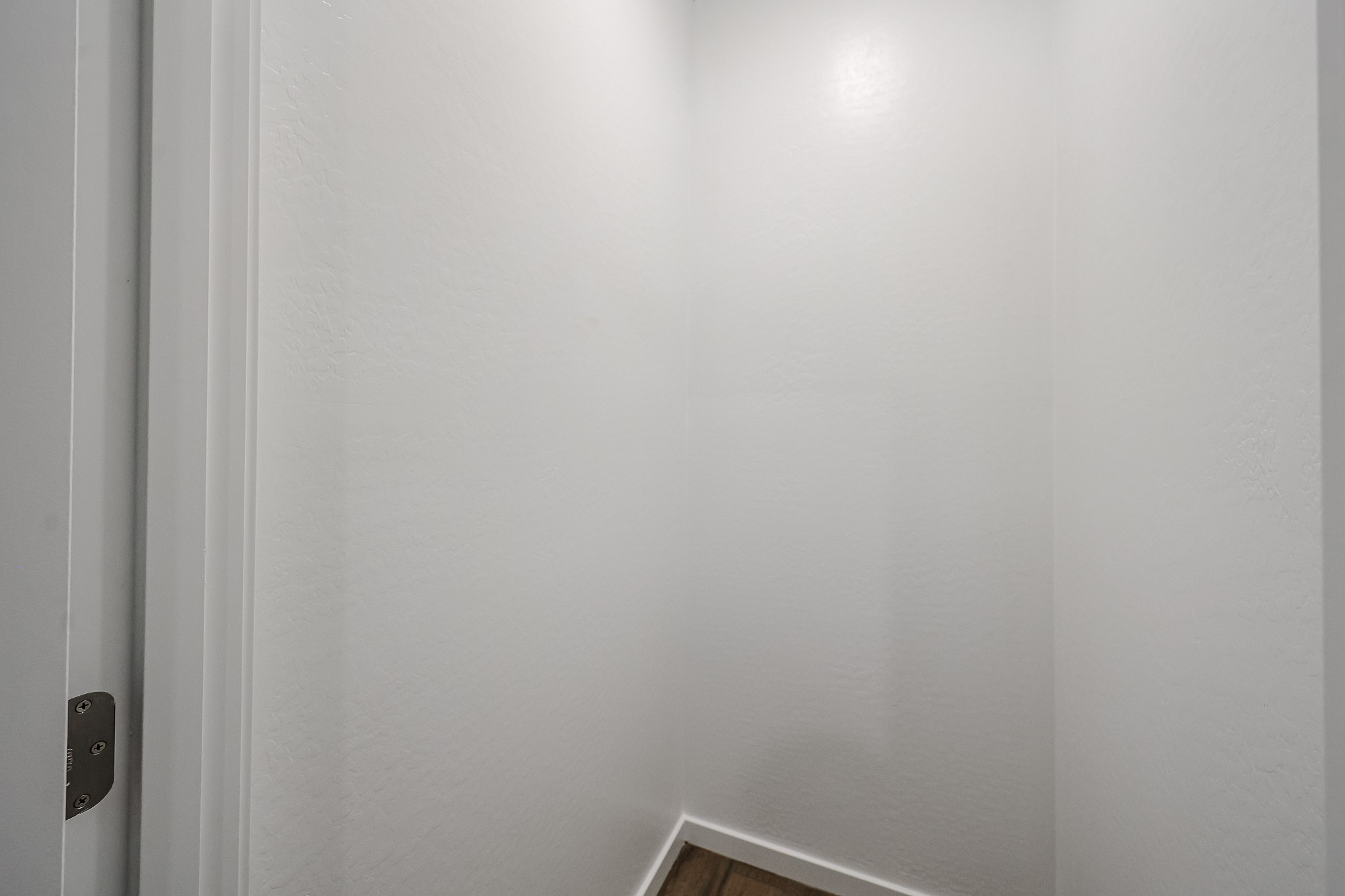 Small, empty, white-walled room with a wood floor and no furniture or decorations, viewed from the doorway.