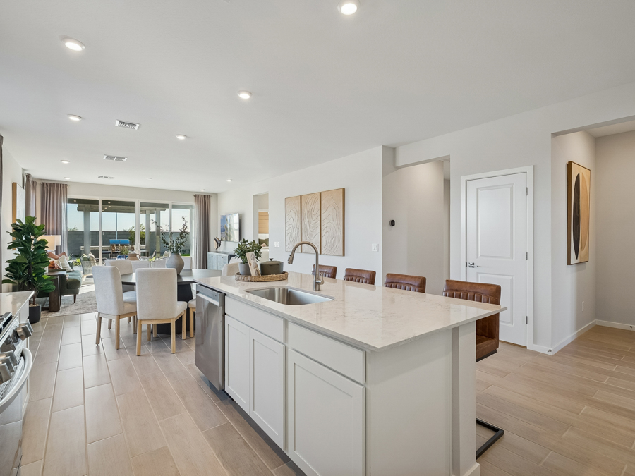 Modern open-concept kitchen and dining area with white cabinets, island, barstools, and large windows leading to a living space.