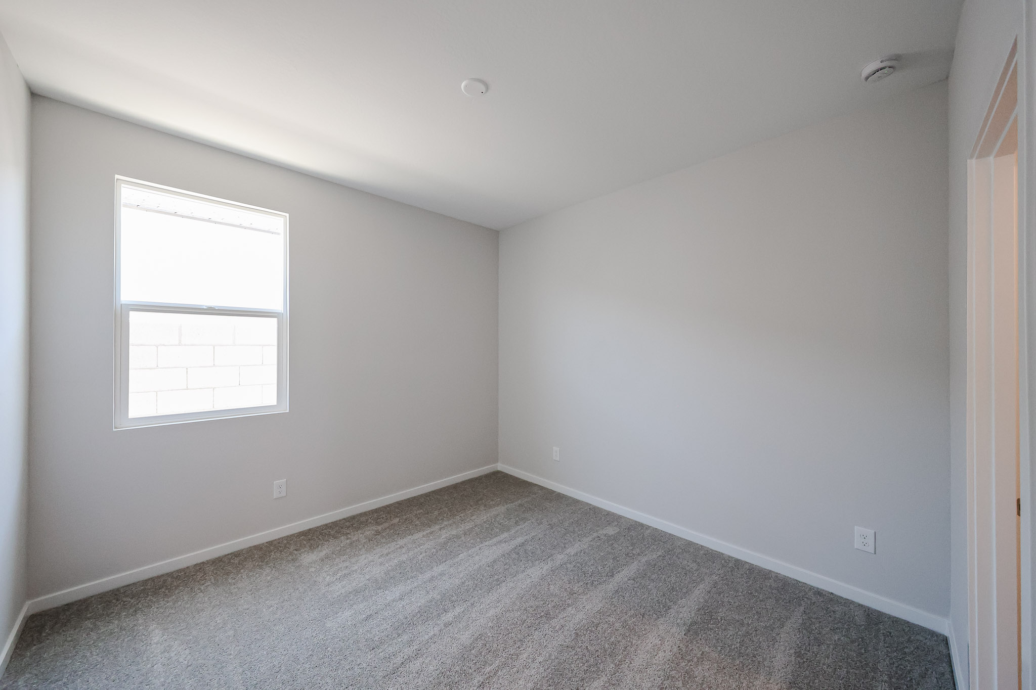 Empty room with light gray walls, carpeted floor, a single window on the left wall, and a doorway on the right.