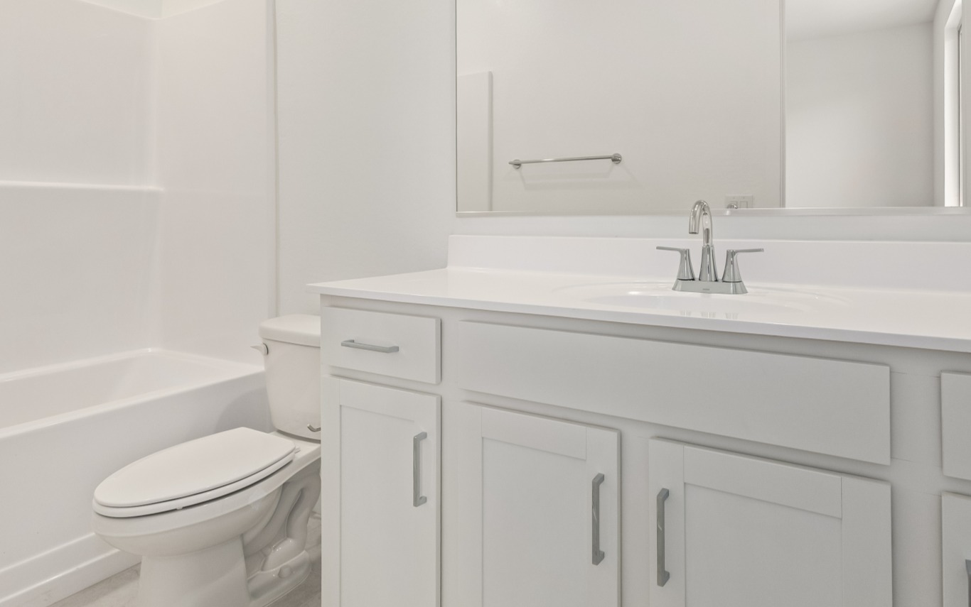 Bathroom with a white vanity, a silver faucet, a wall-mounted mirror, and a toilet next to a bathtub.