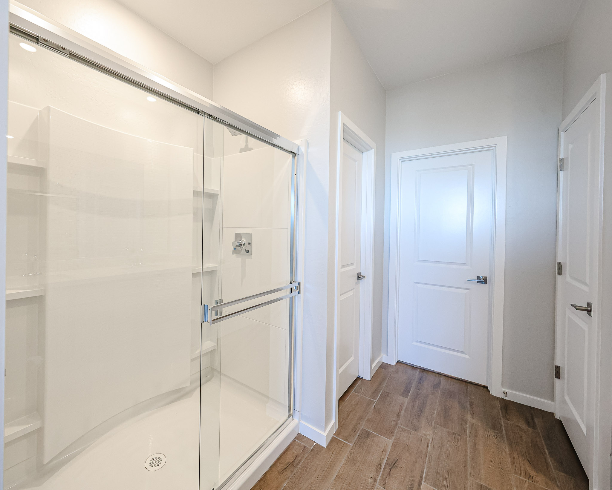 Modern bathroom with a glass-enclosed shower, white doors, light-colored walls, and wood-look tile flooring.