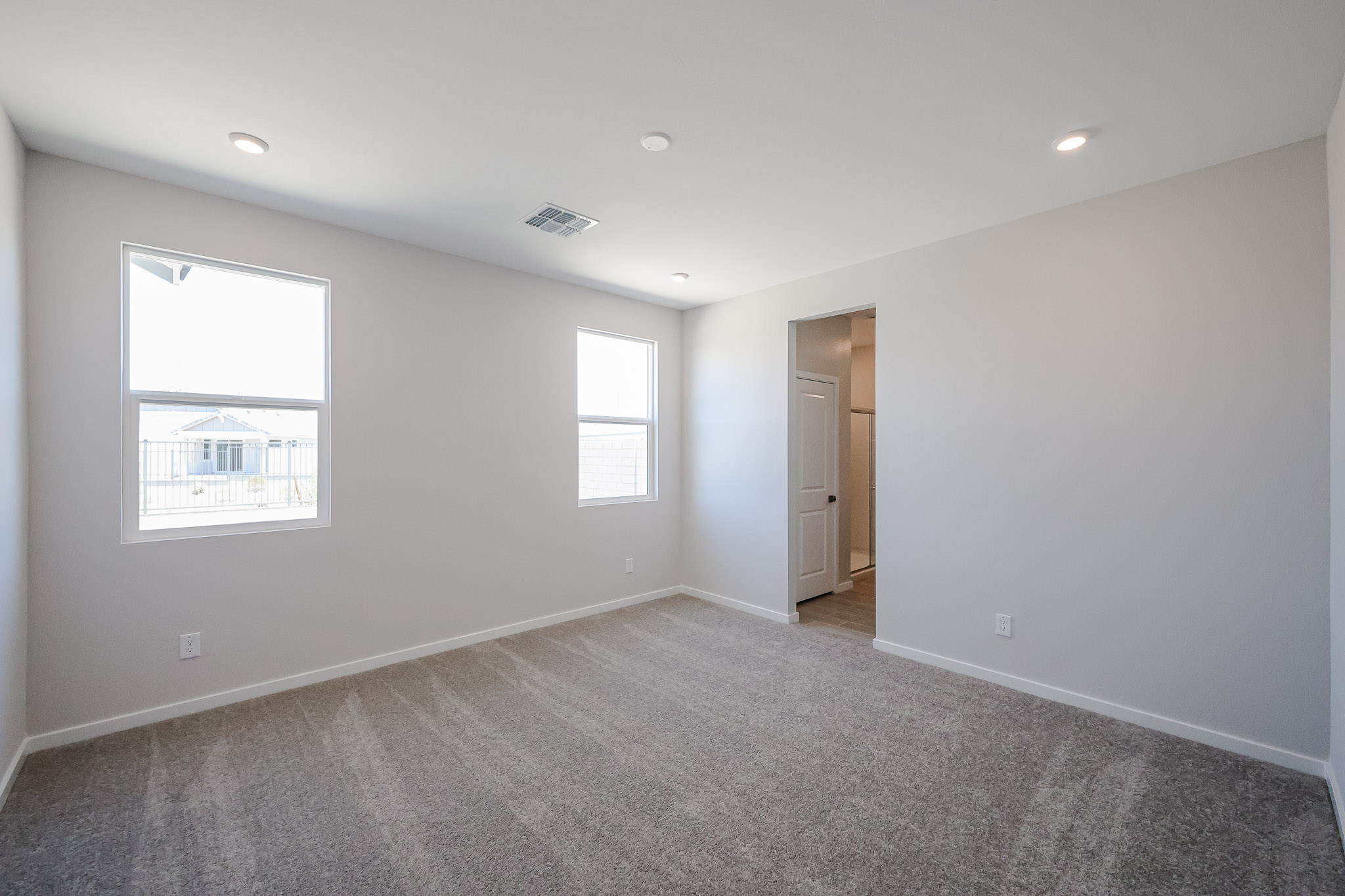 Empty bedroom with light gray walls, two windows, recessed lighting, and carpeted floor. An open doorway leads to a walk-in closet.