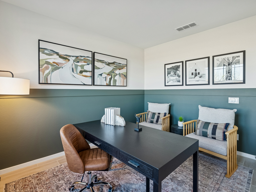 Modern home office with a black desk, brown chair, two armchairs, and abstract art on the wall. The room has green and white walls and a patterned rug.
