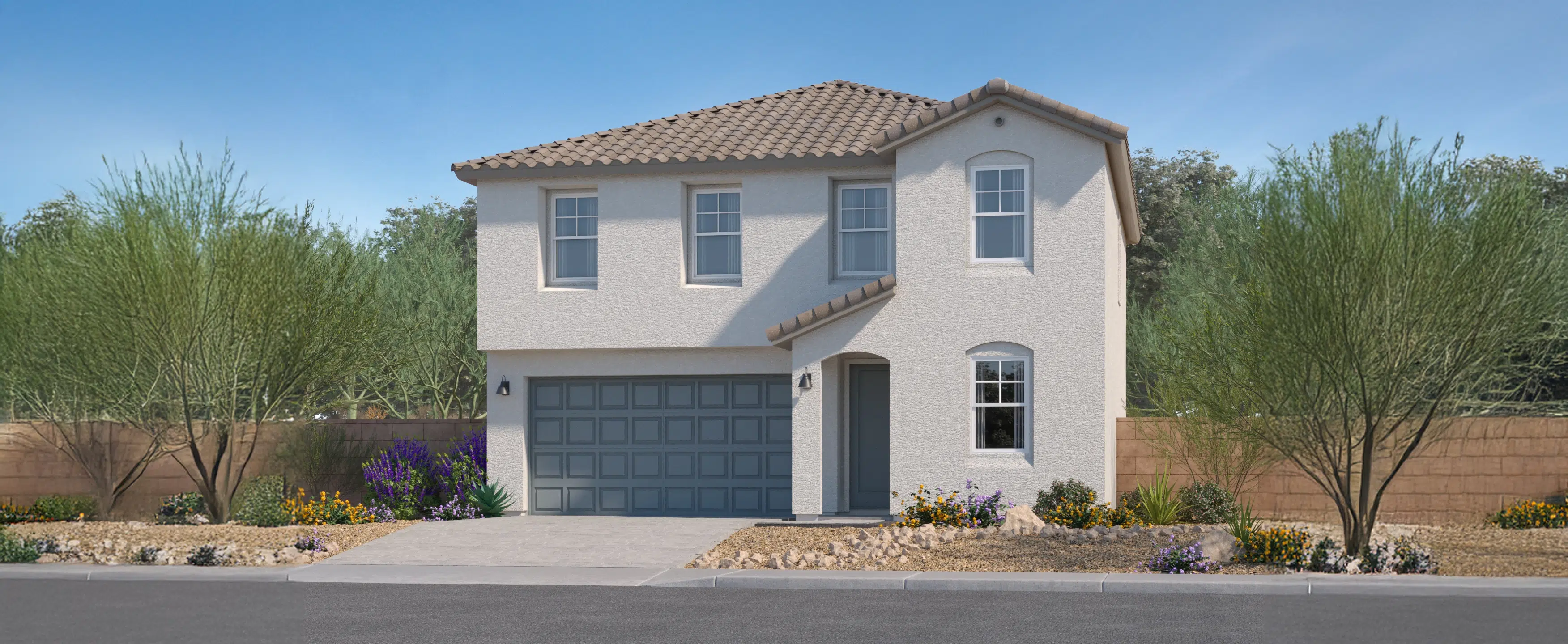 Two-story house with a light stucco exterior, gray tiled roof, two-car garage, and desert landscaping with rocks and drought-tolerant plants.