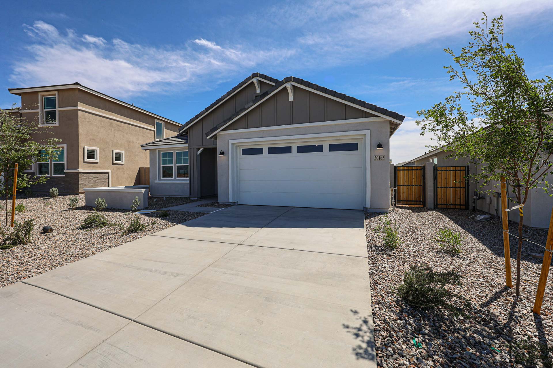 Single-story modern house with a two-car garage, stone landscaping, and a concrete driveway under a blue sky.