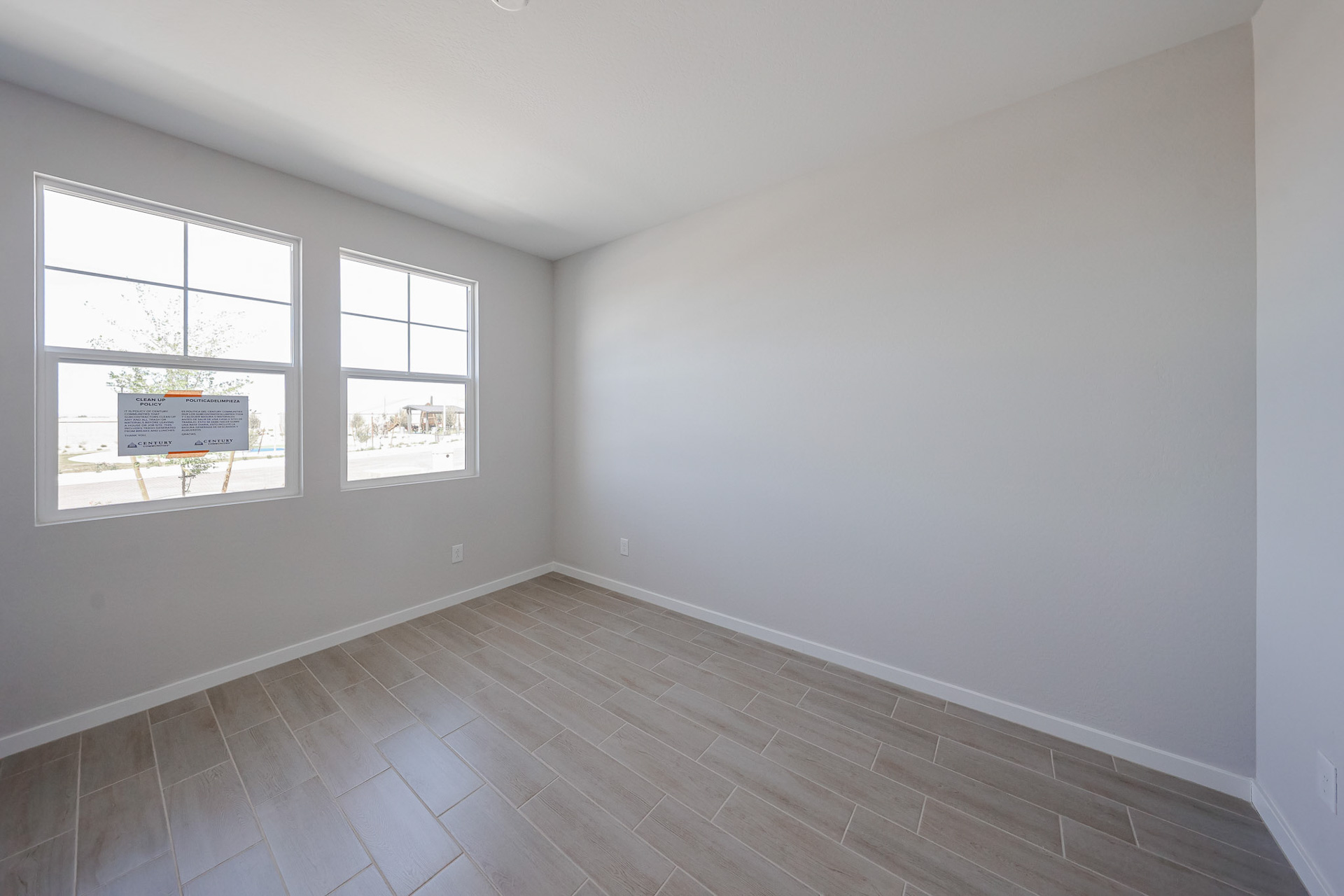 Empty room with light-colored walls, two windows, and wood-look tile flooring. Sunlight enters through the windows, illuminating the simple, unfurnished space.