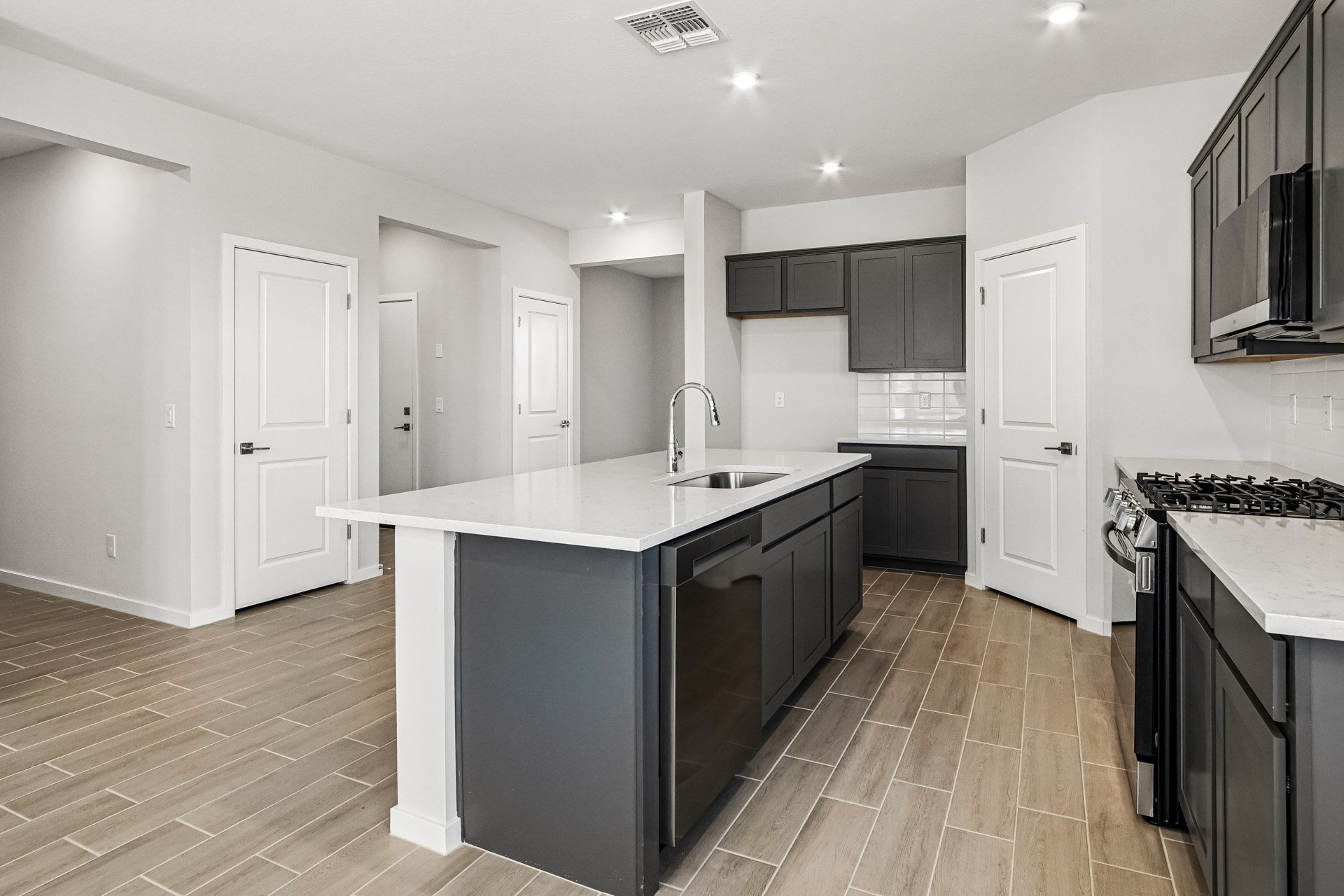 Modern kitchen with dark cabinets, white countertops, center island with sink, tile flooring, and multiple closed doors.