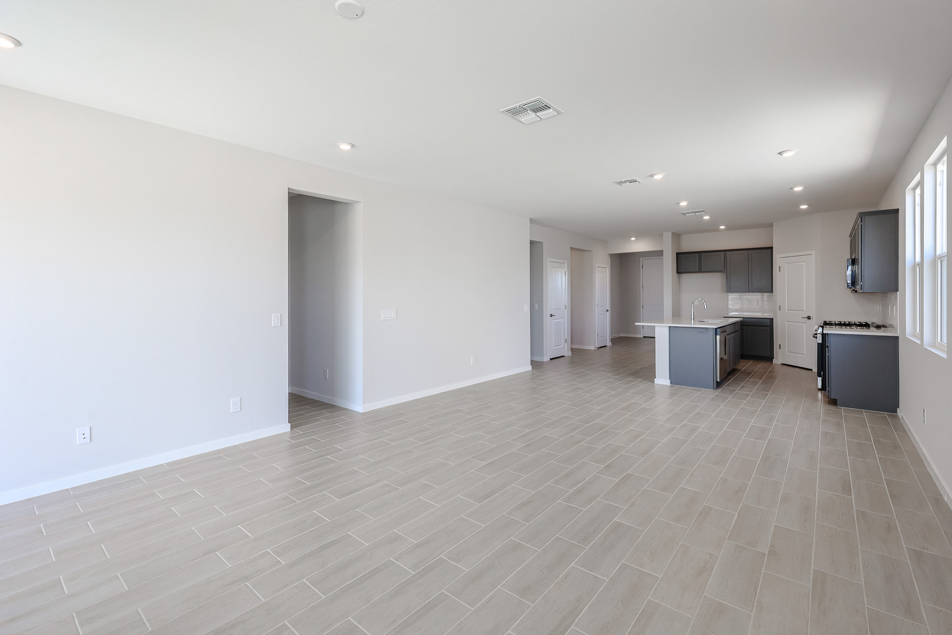Open-concept room with light beige tile flooring, white walls, recessed lighting, and a modern kitchen featuring a center island and grey cabinets.