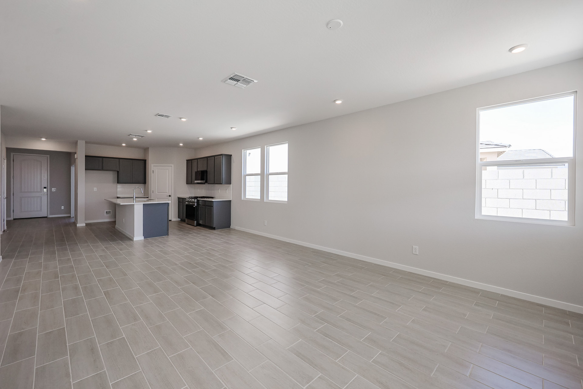 Unfurnished open-plan living area with tiled floors, neutral walls, large windows, and a modern kitchen with gray cabinets and a center island.