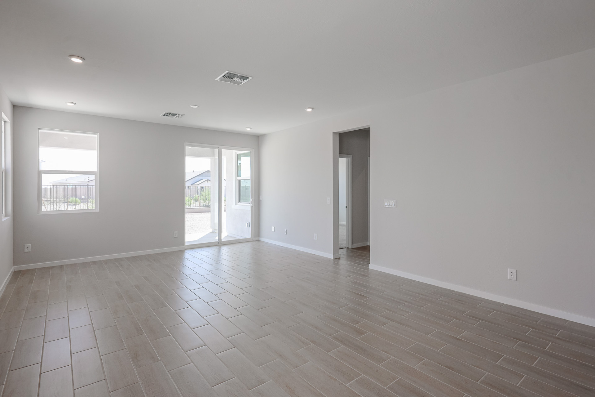 Empty room with light gray walls, beige tiled floor, recessed lighting, two windows, glass doors leading outside, and a doorway to an adjacent space.