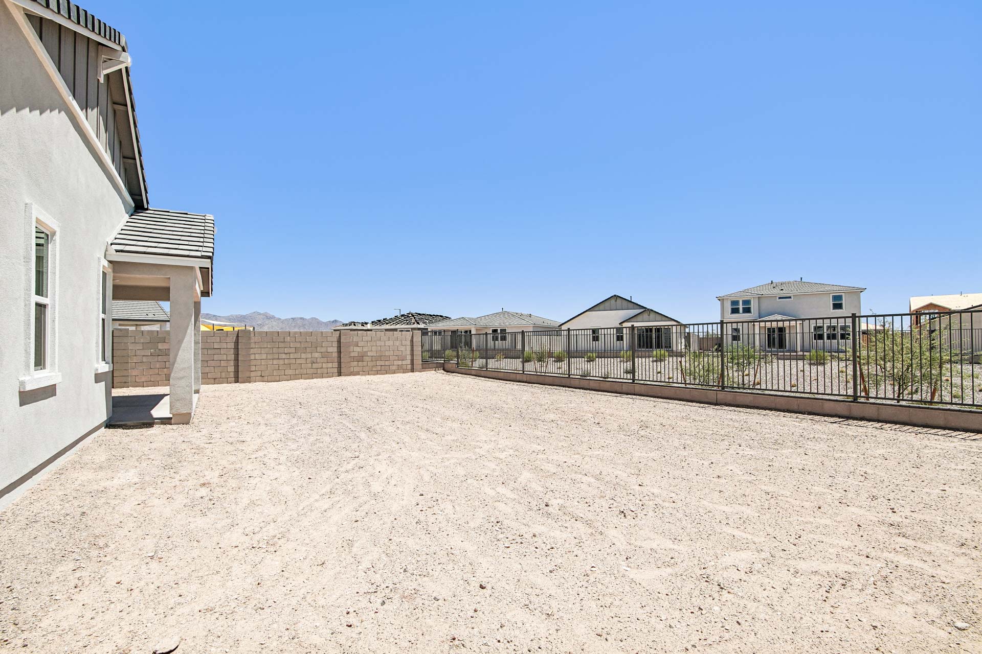 A fenced backyard with bare dirt, next to a light-colored house, surrounded by other modern homes under a clear blue sky.