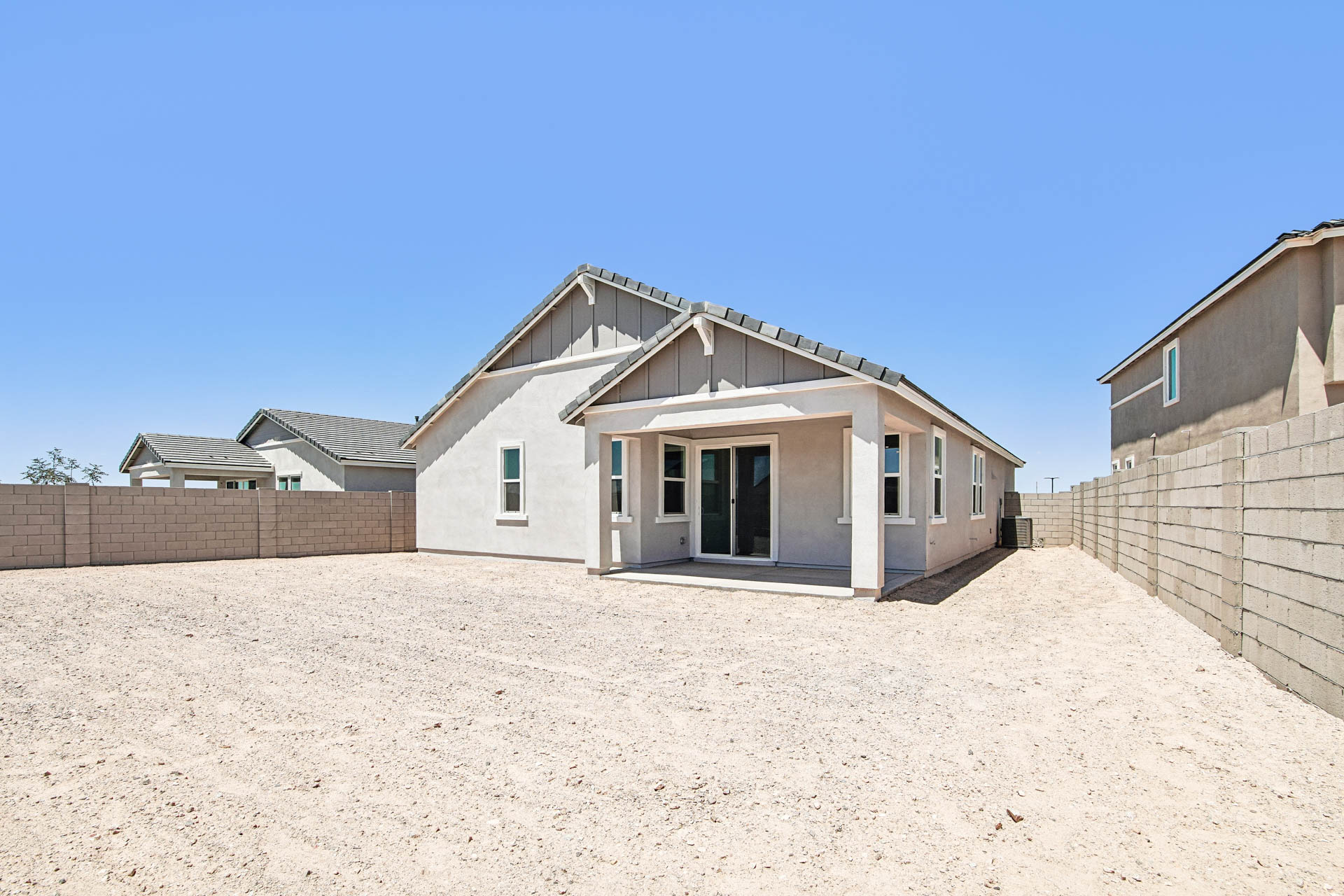 Single-story house with a covered patio and multiple windows, situated in a backyard with gravel landscaping and surrounded by a concrete block fence.