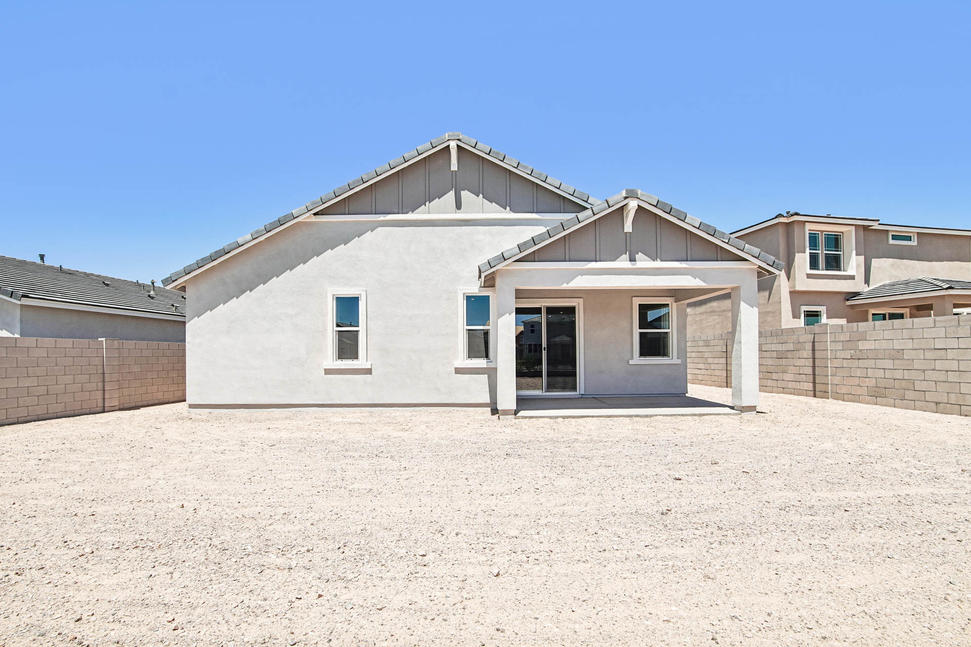 Single-story house with stucco exterior, covered patio, and gravel backyard. The yard is enclosed by a block wall, and neighboring homes are visible.