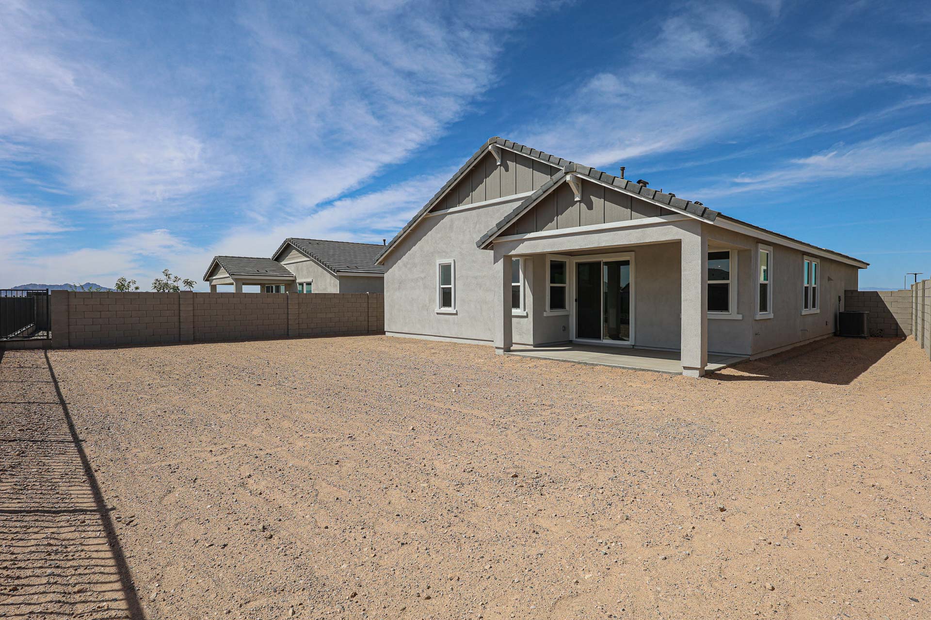 Single-story house with a covered patio and large, bare dirt backyard enclosed by a block wall under a blue sky.