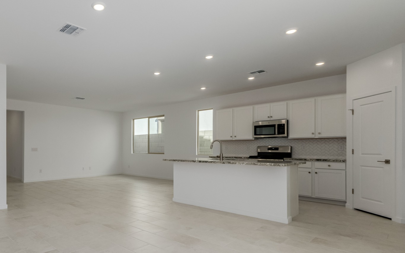 Modern, unfurnished open-concept kitchen and living area with white cabinets, stainless steel appliances, and tiled floors. Large windows provide natural light.