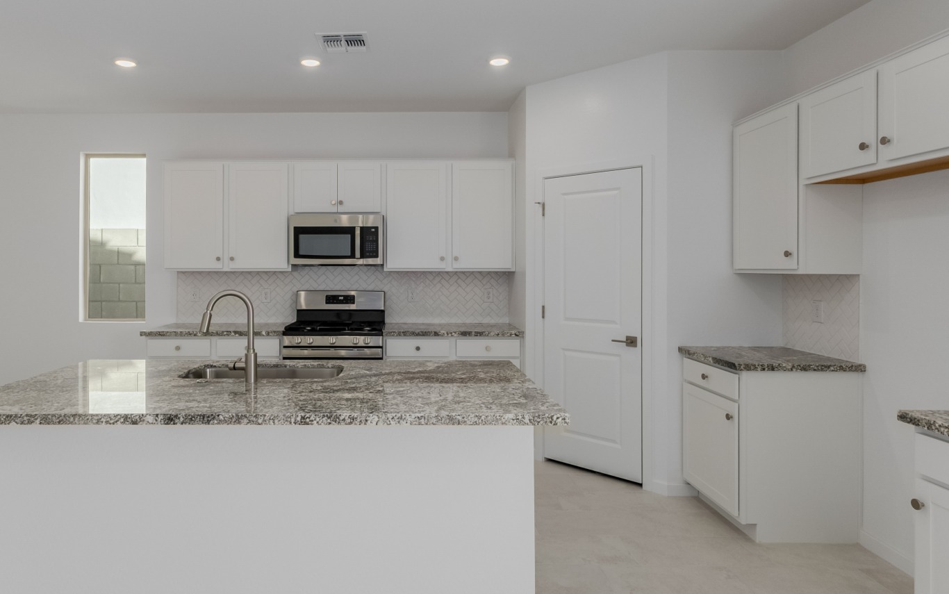Modern kitchen with white cabinets, stainless steel appliances, granite countertops, an island with a sink, and recessed lighting.