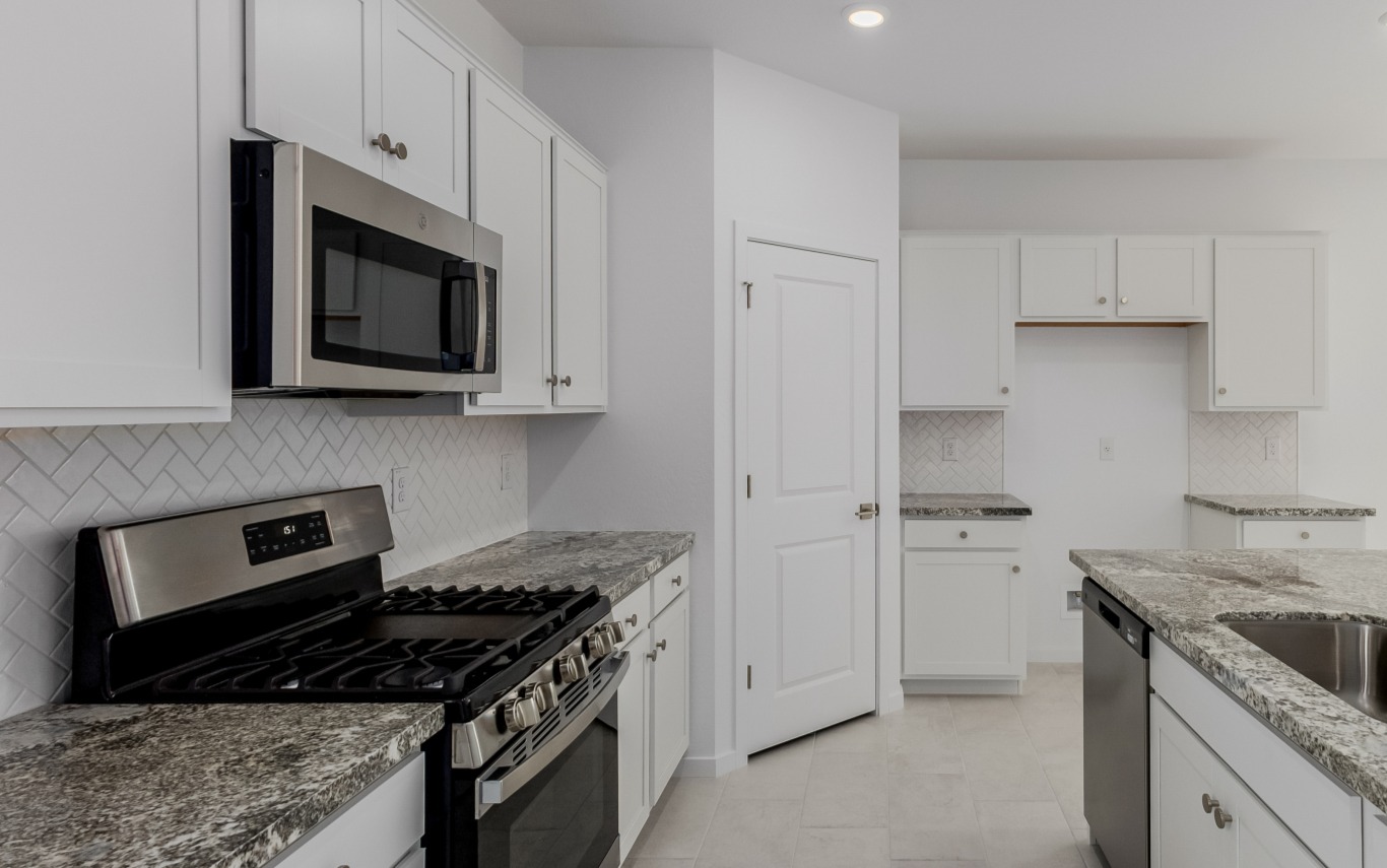 Modern kitchen with white cabinets, stainless steel appliances, granite countertops, a gas stove, an over-the-range microwave, and a central island with a sink.